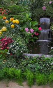 Professional two-tier waterfall fountain and pond installation surrounded by vibrant floral landscaping in a Des Moines backyard.