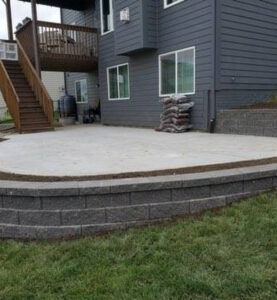 a light gray concrete patio surrounded by a dark gray retaining wall behind a dark gray house