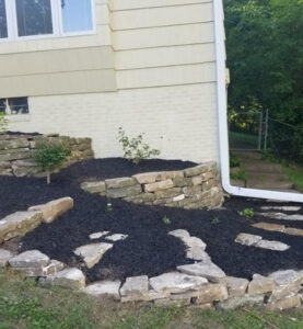 new landscaping in front of a house featuring stone retaining walls, small plants, and dark mulch