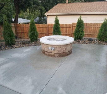 Custom circular tan brick fire pit on a professional concrete patio with evergreen privacy landscaping in Des Moines.