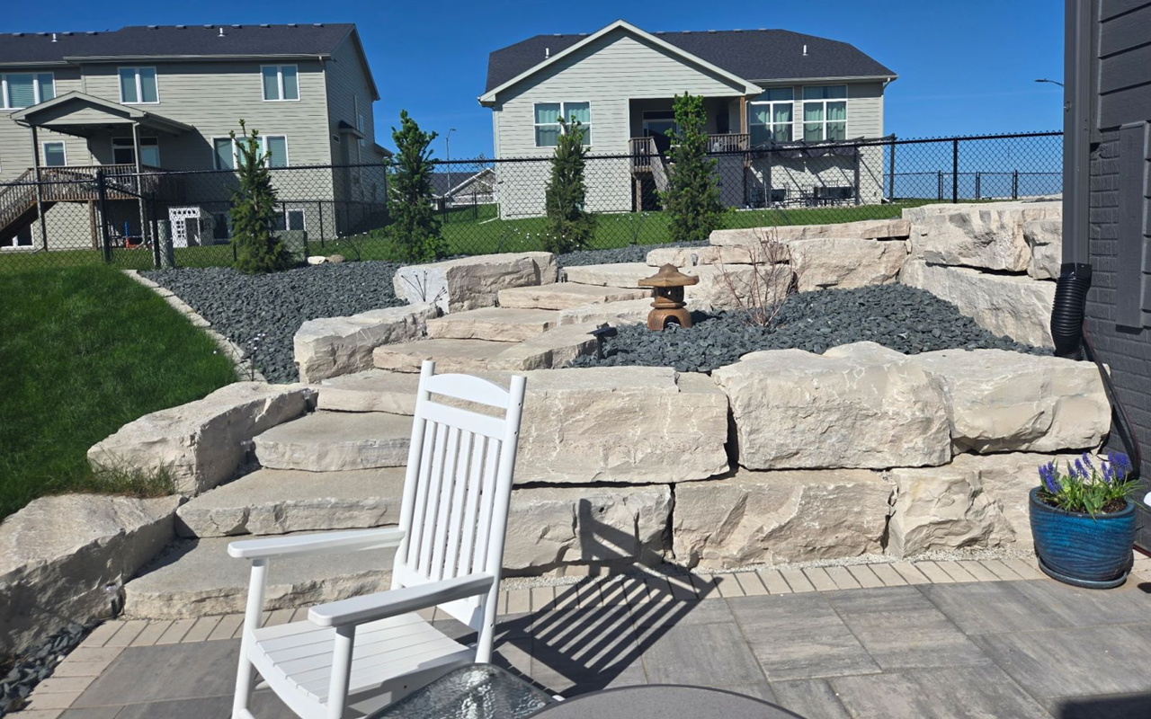 Natural boulder retaining wall with built-in stone stairs installed by hardscape contractors in Ankeny, Iowa.